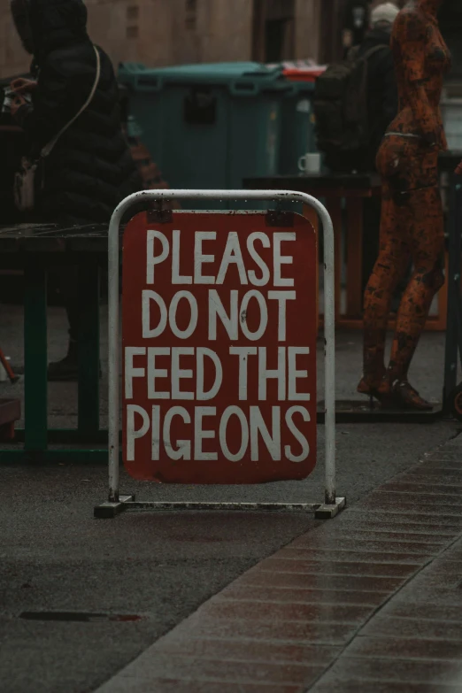 a sign stating please do not feed the pigeons on a city street