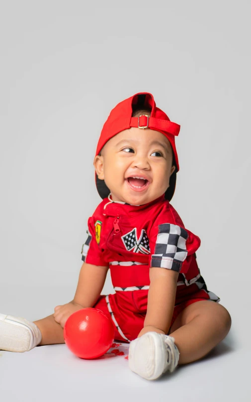 a baby wearing a race uniform sitting on the floor with a smile