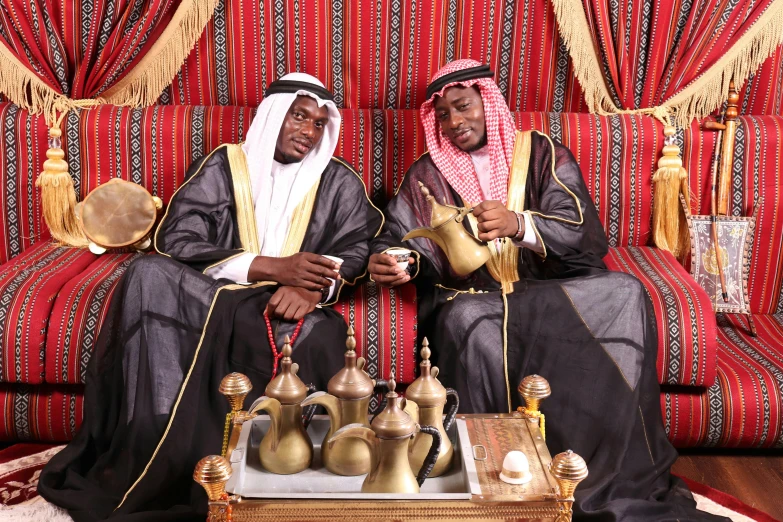 two men sitting on a couch, one holding coffee pot