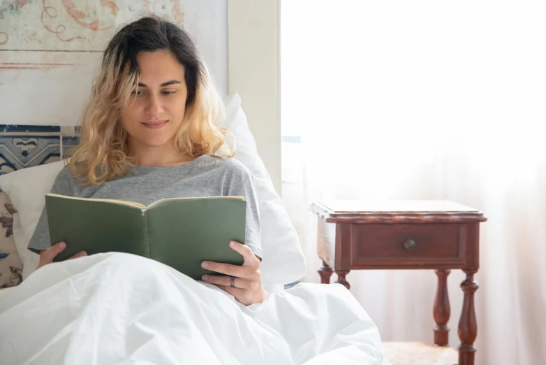 a woman reading a book while laying in bed