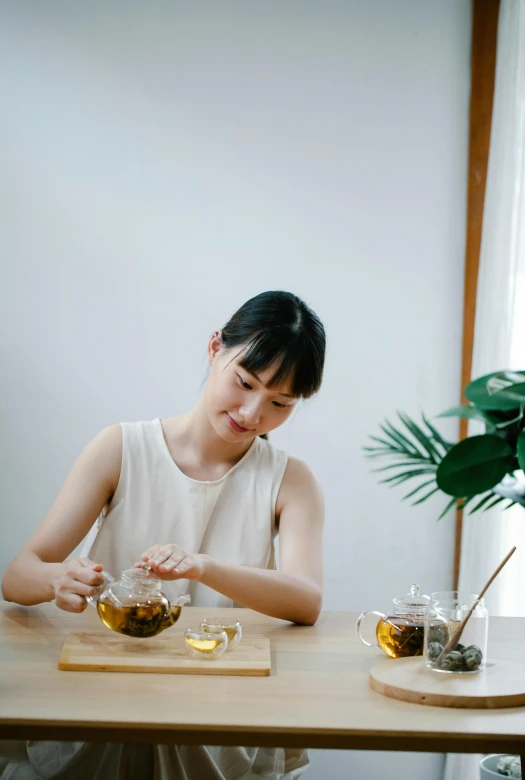 a woman sitting at a wooden table in front of a tea pot