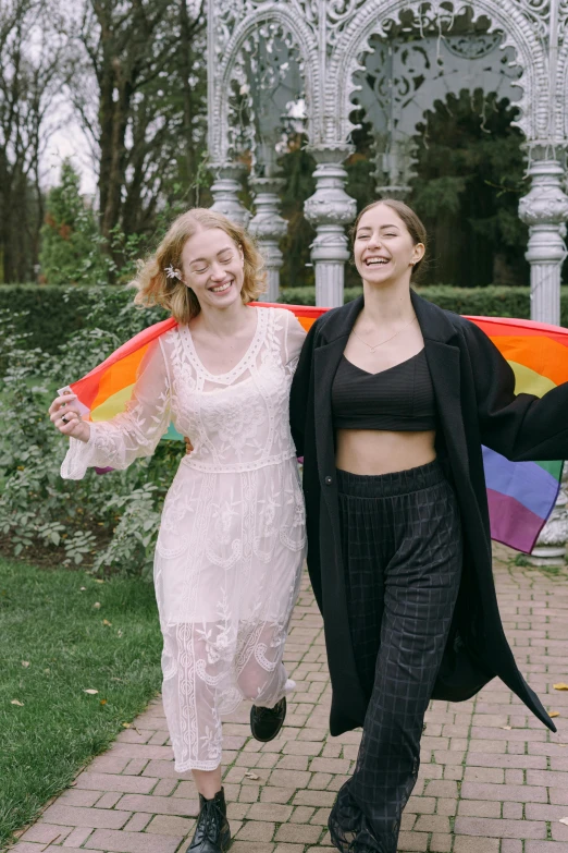 two young women are smiling while carrying rainbow kite