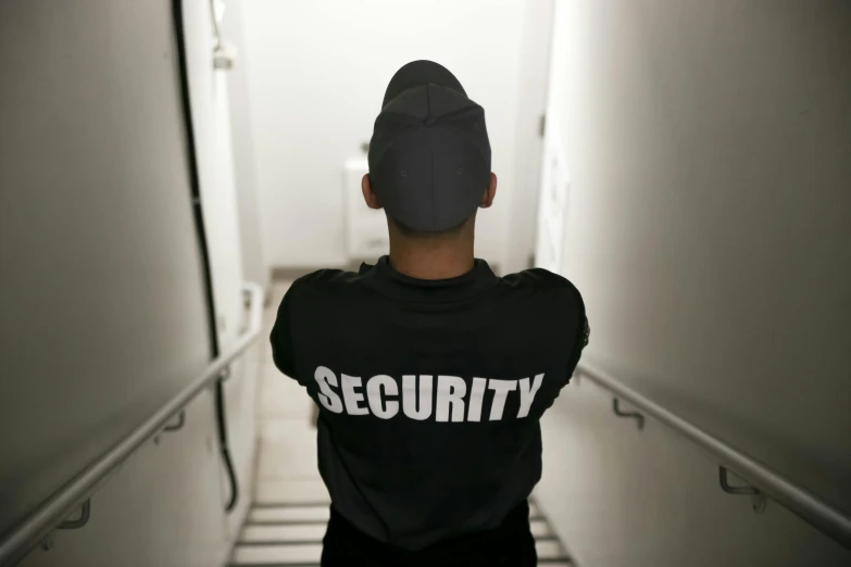 a man standing in a hallway wearing a security shirt