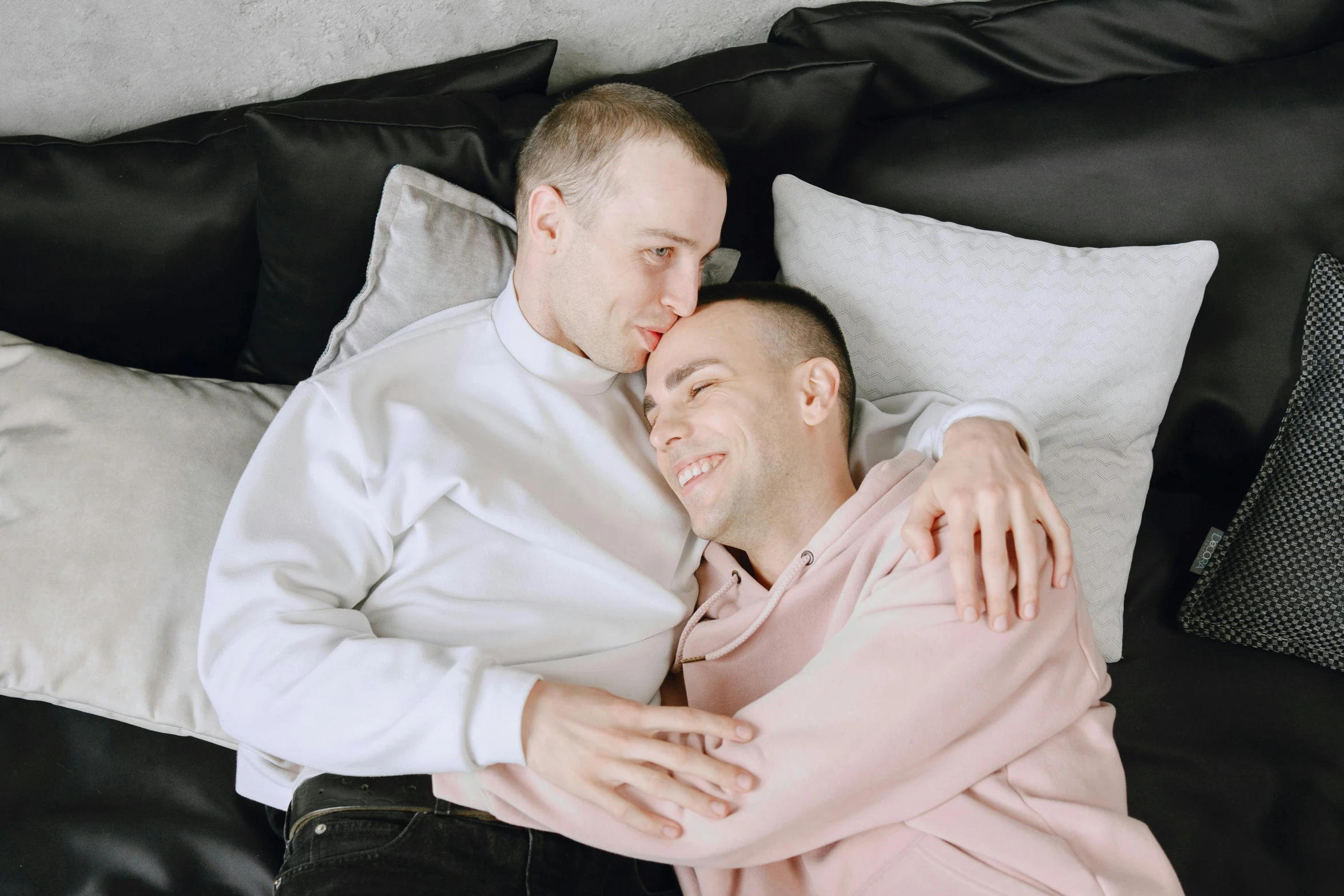 two men who are laying on a bed hugging