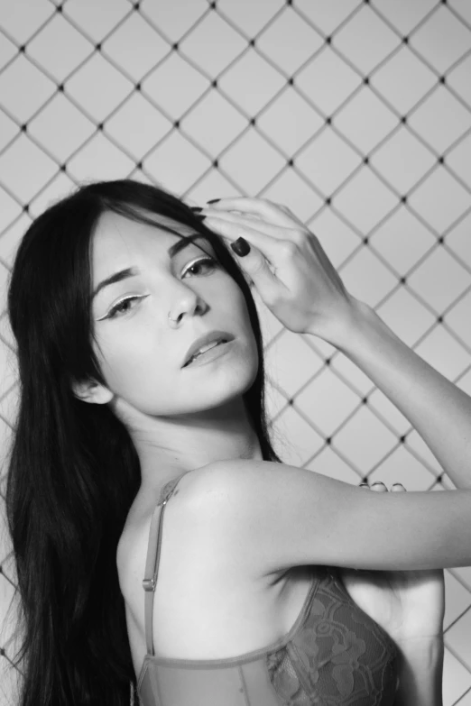 a young lady poses in front of a fence with her hand up to her hair