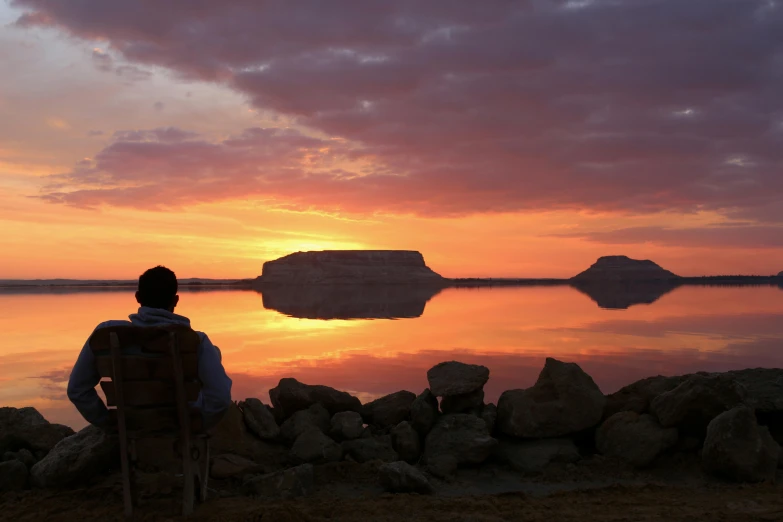 a person is standing on a rock cliff overlooking a lake with some large rocks