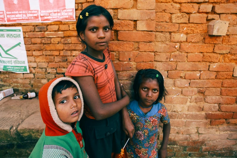 four children standing near a brick wall