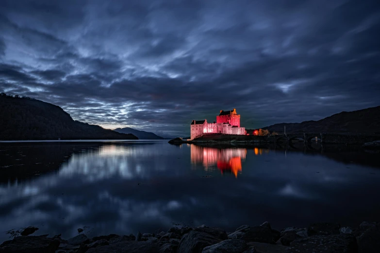 the night sky over a lake with a red castle in it