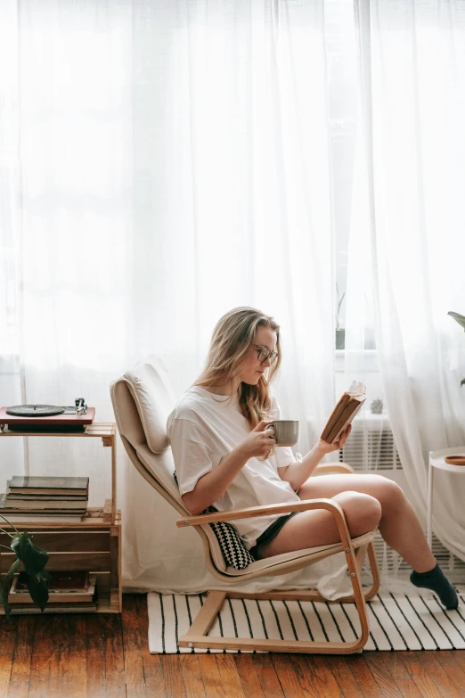 the young woman is sitting in a rocking chair and reading a book