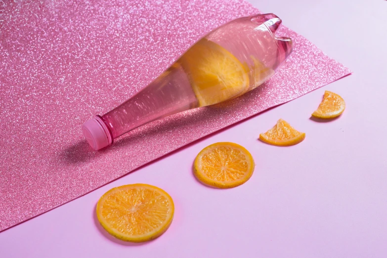 several orange slices and one bottle sitting on a pink surface