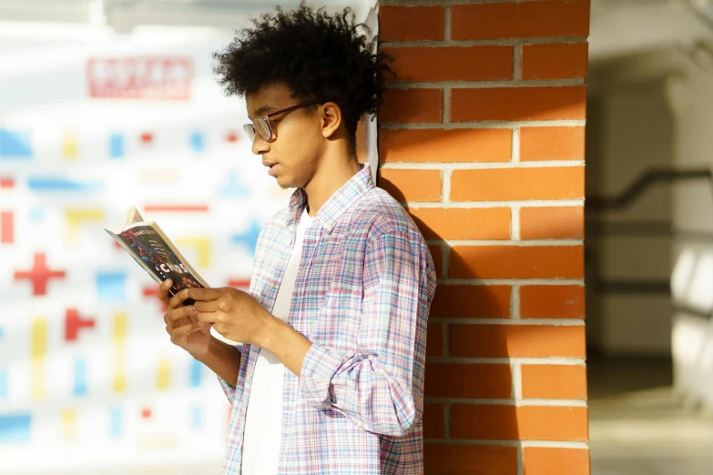 a man wearing glasses and reading on a brick wall