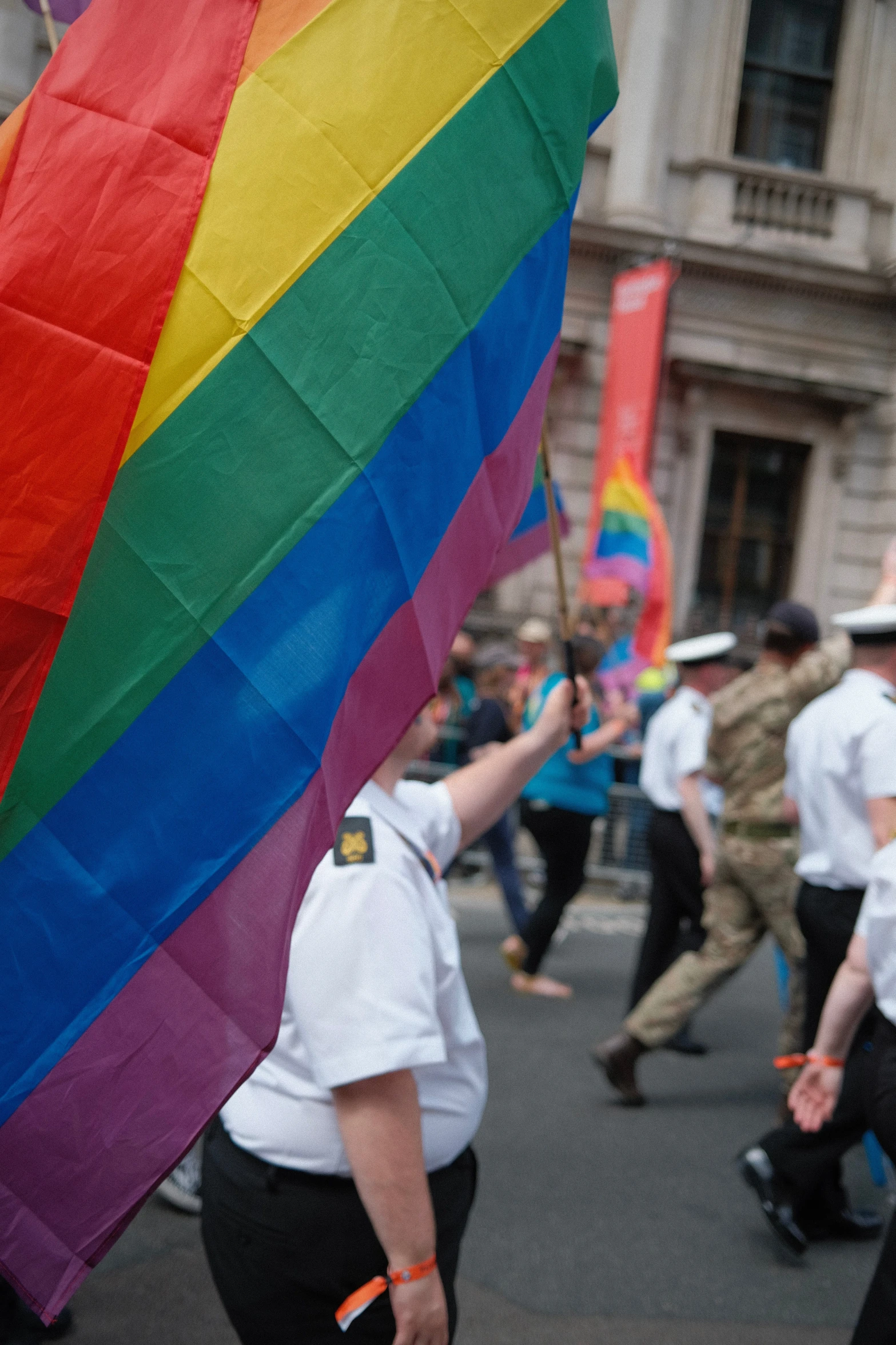 many people with uniforms and balloons are holding a rainbow flag