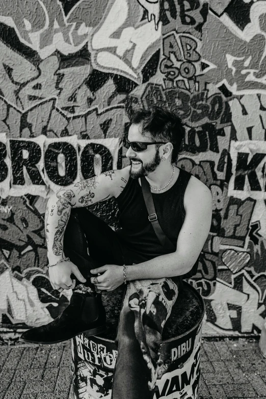 a young man is sitting on a ledge wearing sunglasses and tattoos