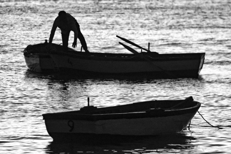 two small boats are on the water with a man working