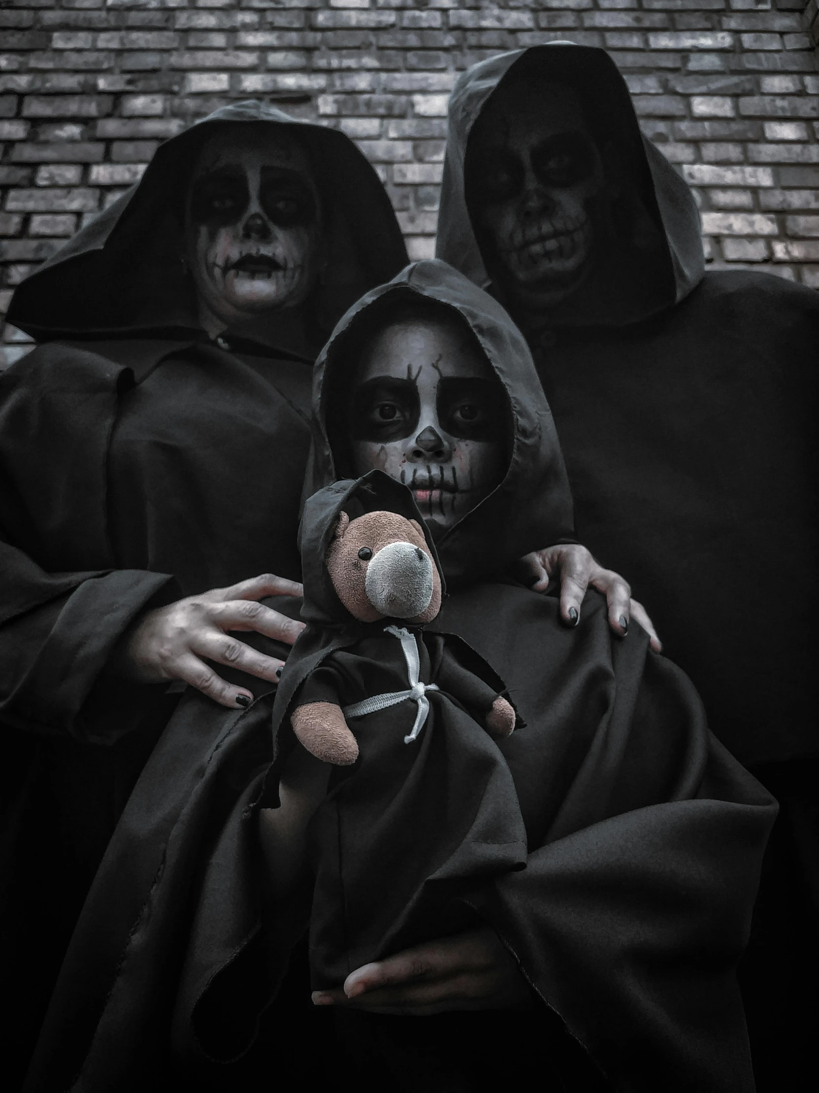 three people in hooded clothing holding a small teddy bear