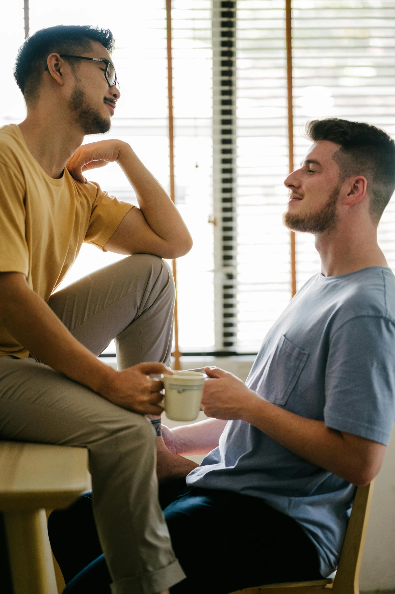 two men sitting on the couch one drinking from a coffee cup