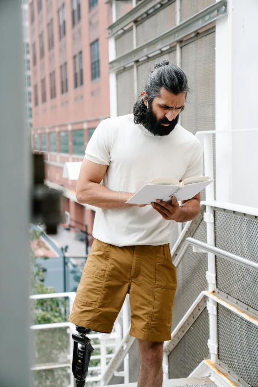 a man with an unusual leg ce standing near a rail and reading a book