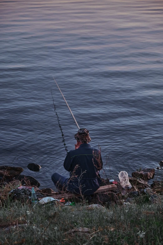 a man sits near a body of water while fishing
