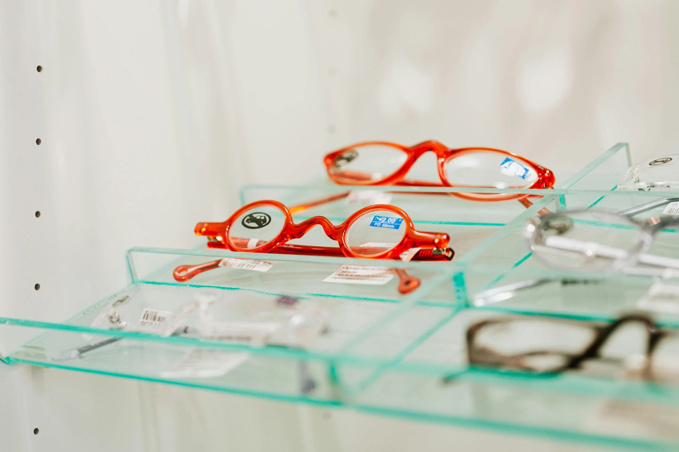 a pair of red reading glasses sit on three clear shelves