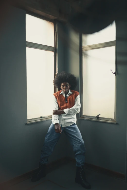 young man leaning on the corner of an empty room with windows in it