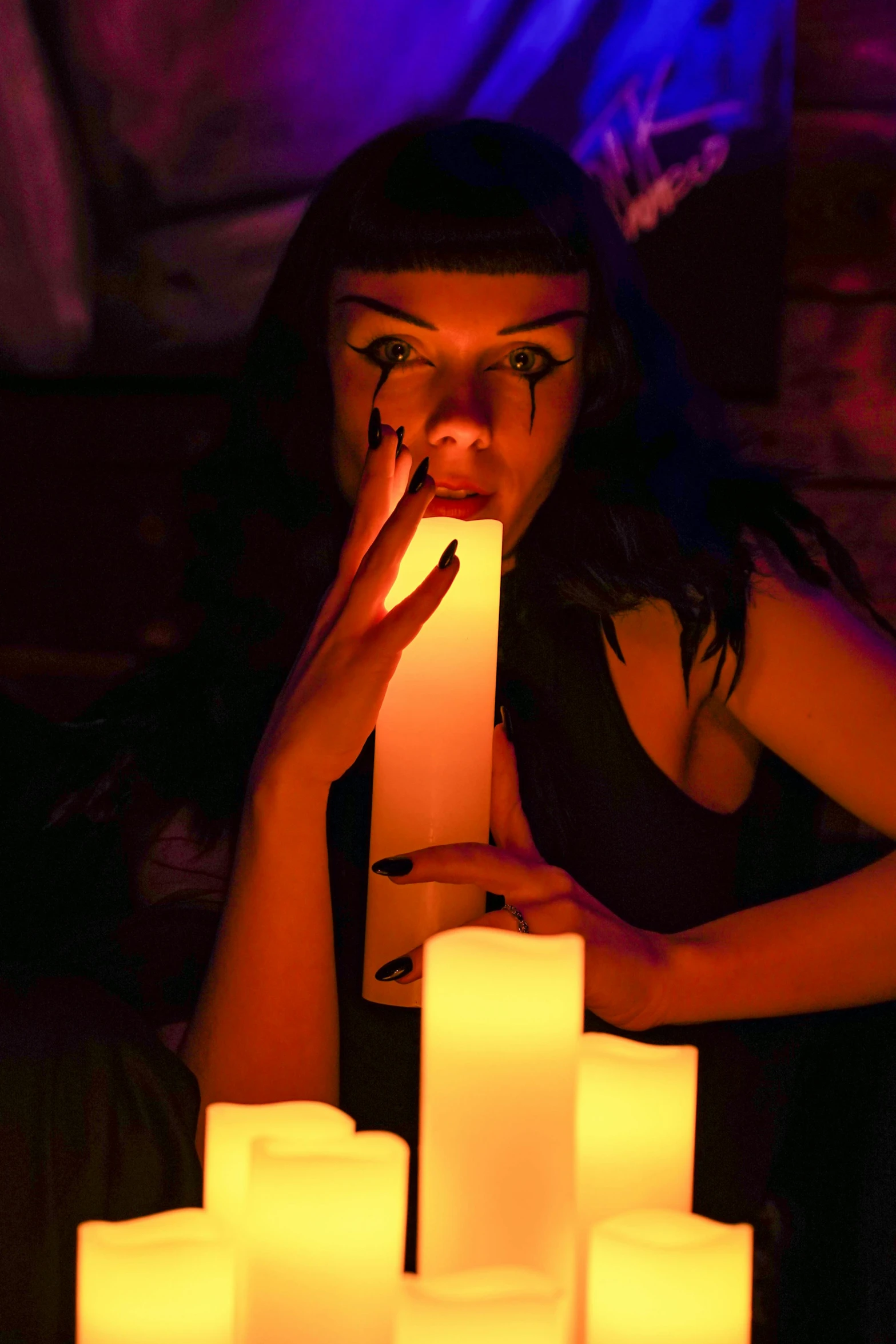 a woman with her face painted as evil looking, sits in front of candles