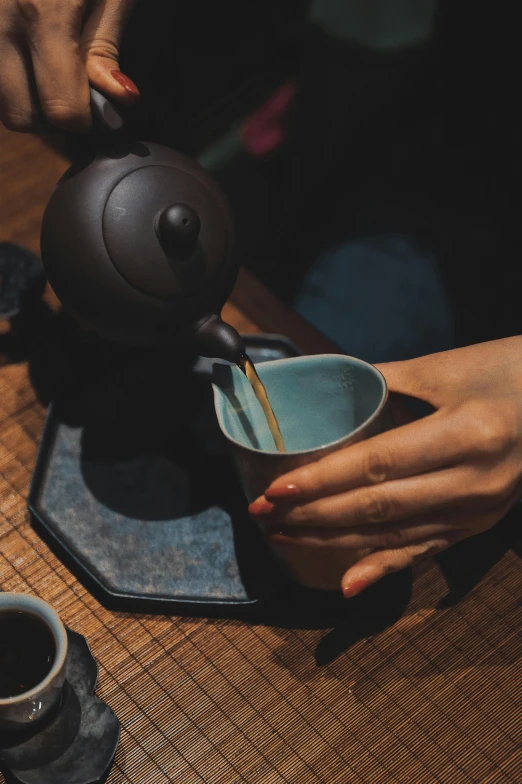 a person pours a cup of tea into a blue tea pot