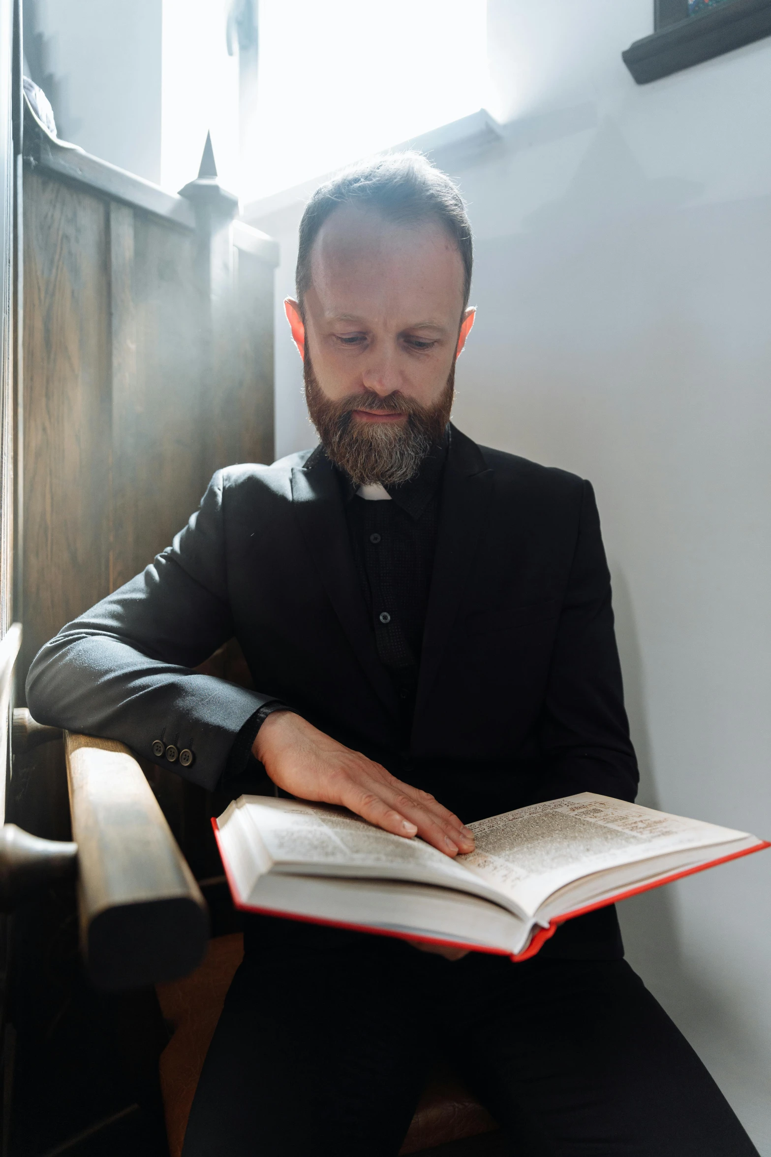 bearded priest holding open bible while sitting down