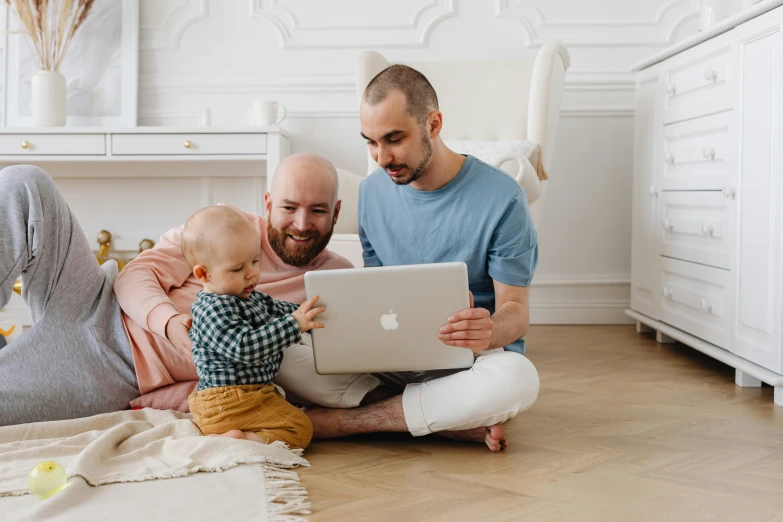 two men are playing with a laptop while a baby watches