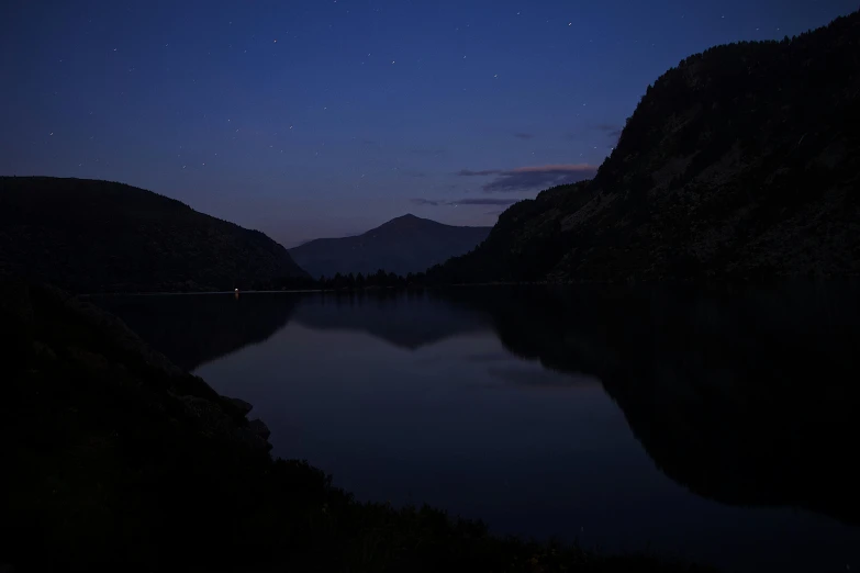 a clear lake and mountains at night with stars in the sky