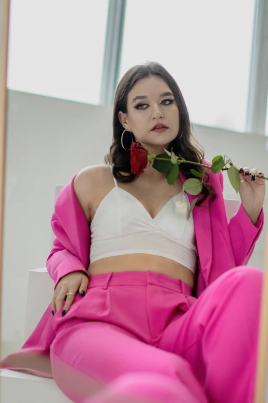 a woman wearing pink pants and a white top sitting next to a rose