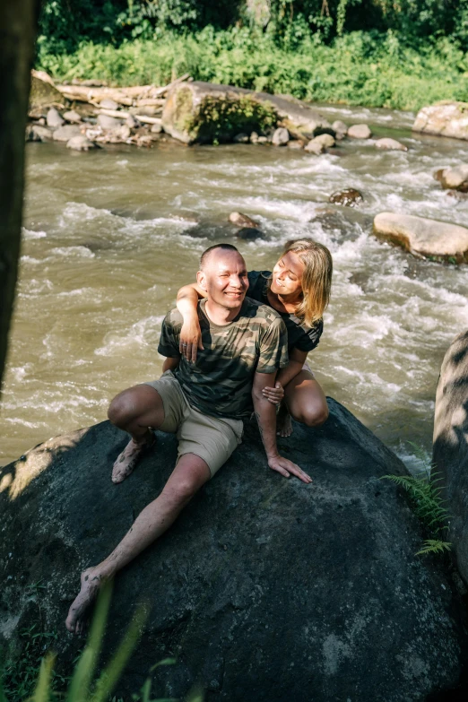 a man and a woman sitting on a rock in the middle of the river