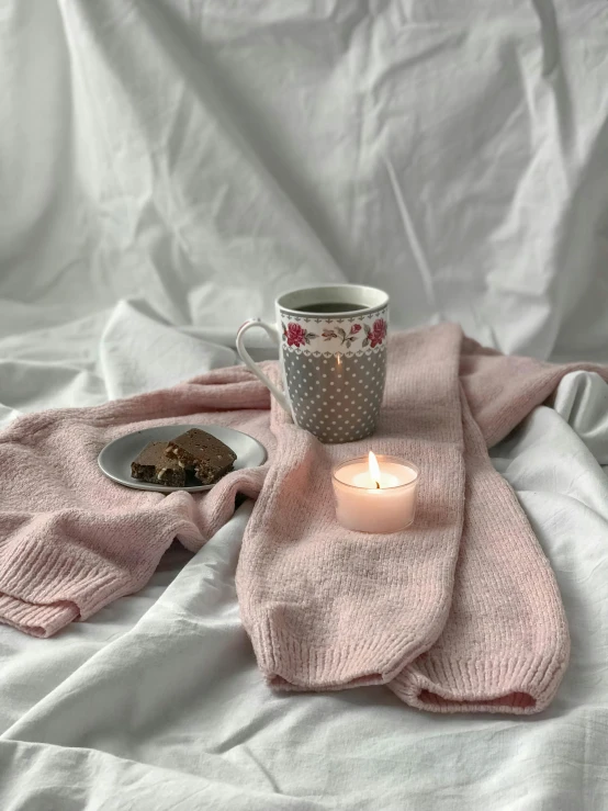 a candle in front of a cup on a blanket