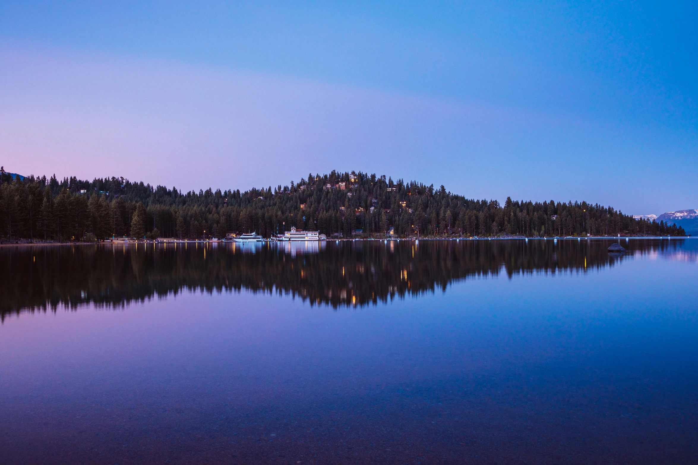 a calm lake in the early evening with boats floating on it