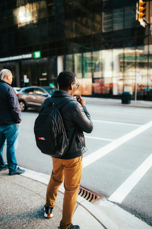 man in black jacket walking down the sidewalk on his cell phone