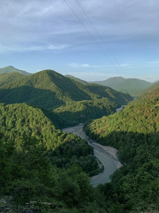 a stream flowing between green mountains under a blue sky