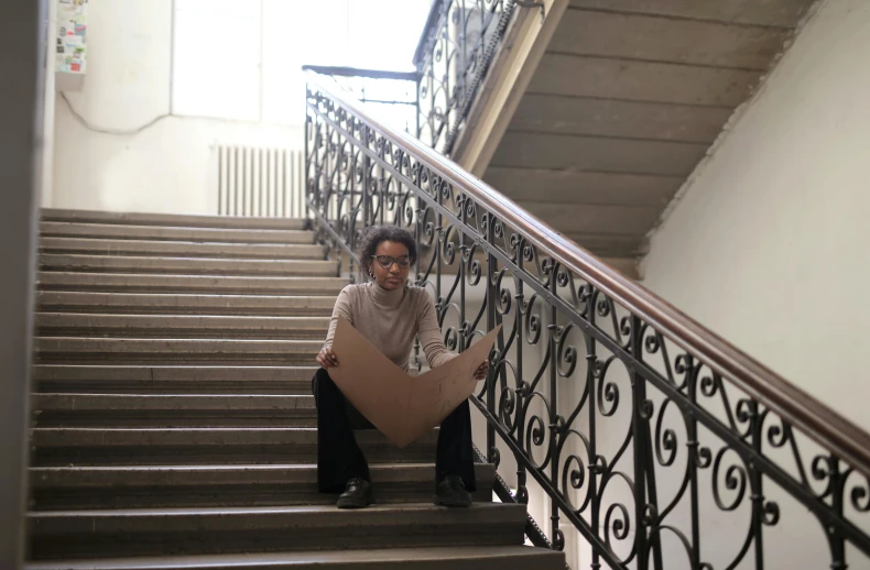 woman sitting on a stair case with a piece of cardboard over her stomach