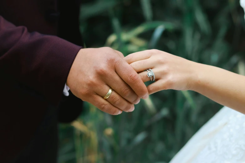 the bride holds her wedding ring with her groom's hand