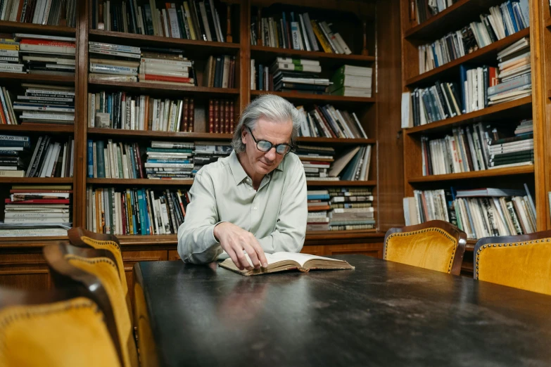 man reading a book while sitting at table in liry