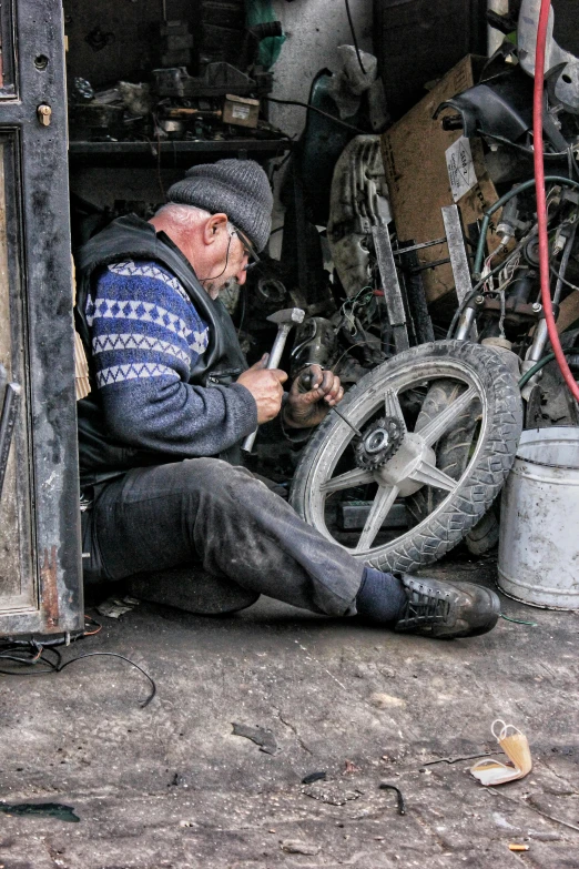 an old man working with soing while sitting under a wheel