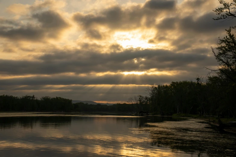 a calm water at sunset with light beaming from the clouds