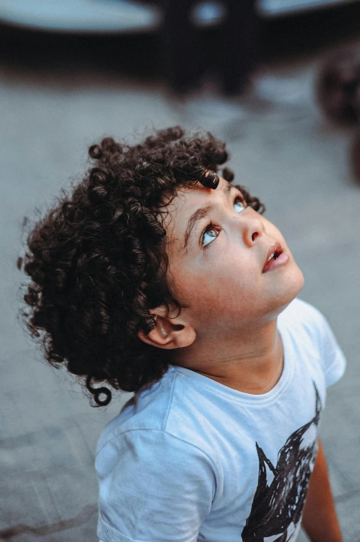 little boy with curly hair looking up on street