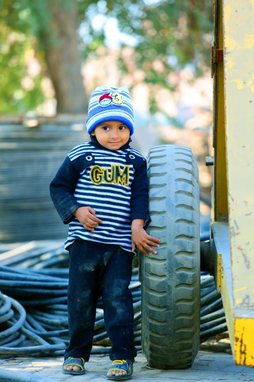a toddler boy posing beside a large tire