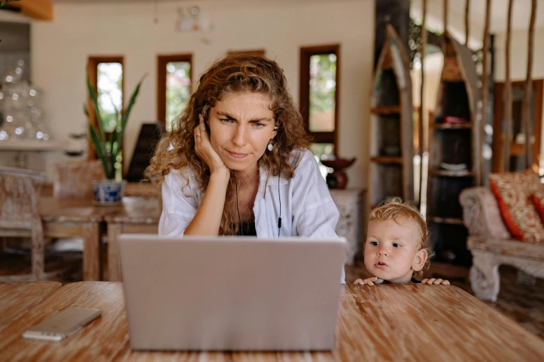 a woman sitting at a table with her child and using a laptop