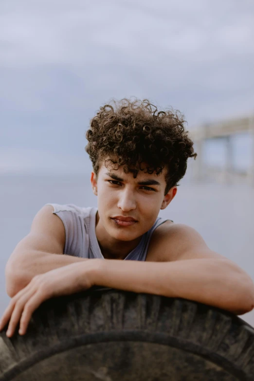 a  with curly hair leaning on a tire