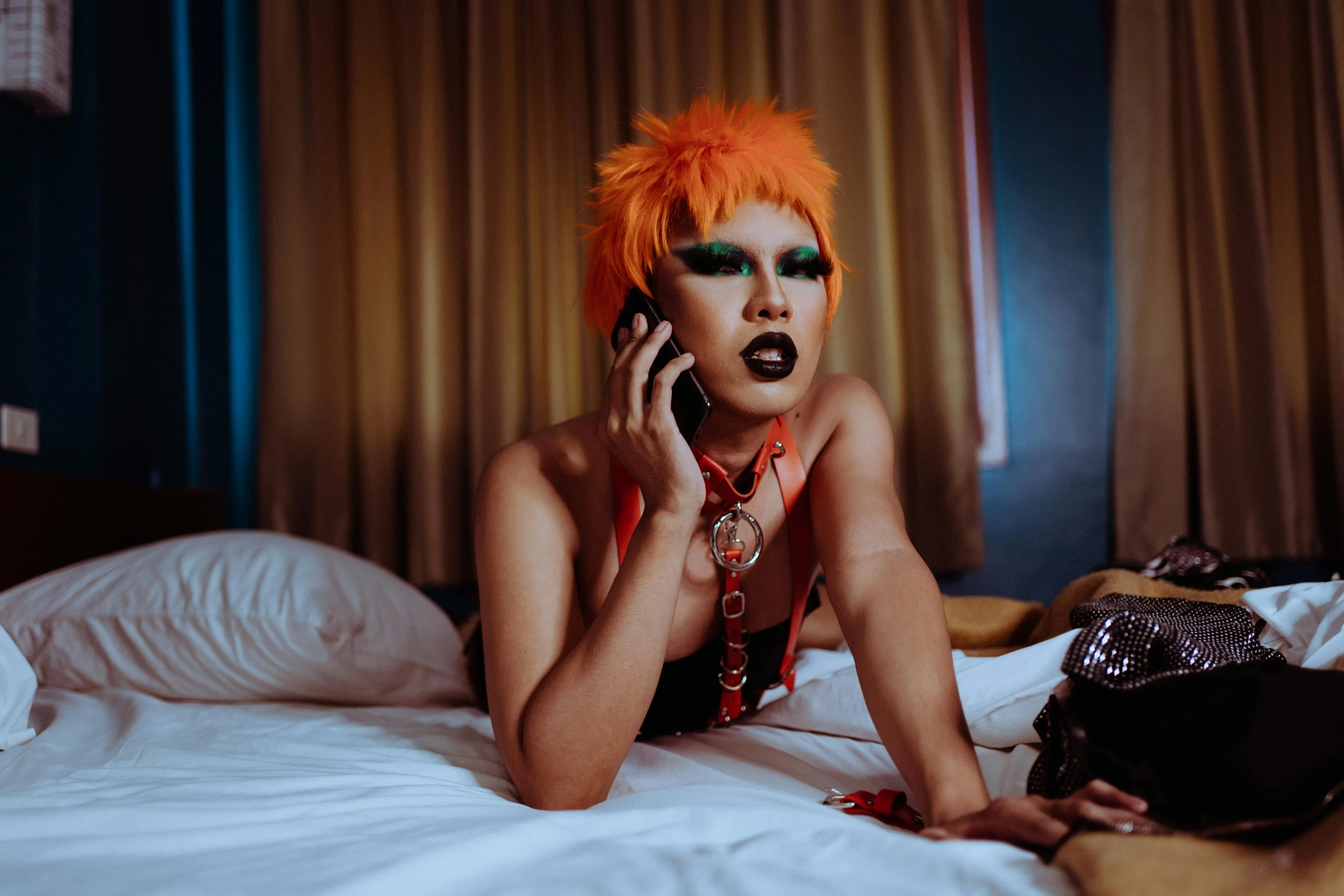 woman with bright orange hair laying on bed and talking on cell phone