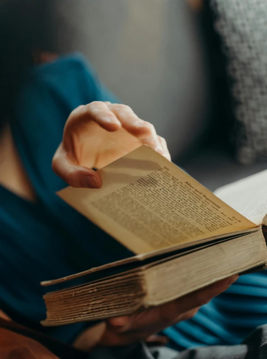 someone holding out an open book while sitting on a couch