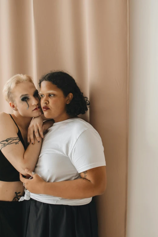 two women that are emcing each other while standing by a wall