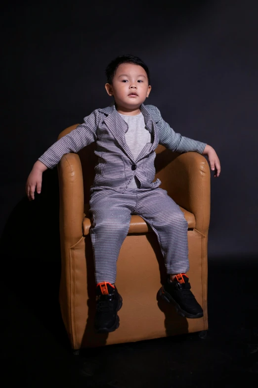small child in black suit and tie sitting on chair