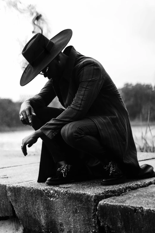 black and white pograph of man wearing long coat, tie, and hat