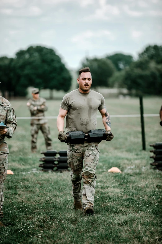 four military men carrying large objects through the field